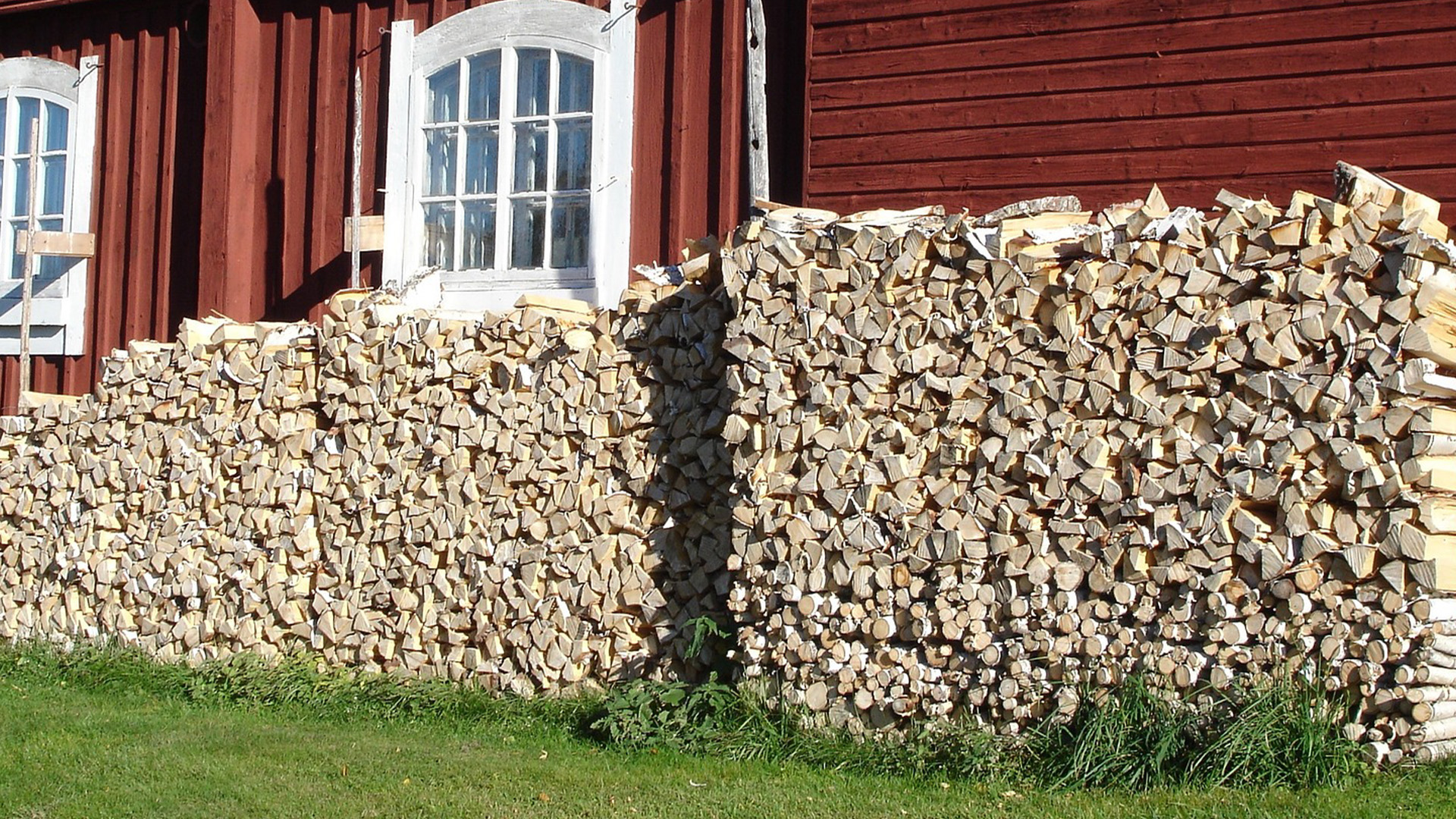Two large wood piles stacked against the exterior of a home